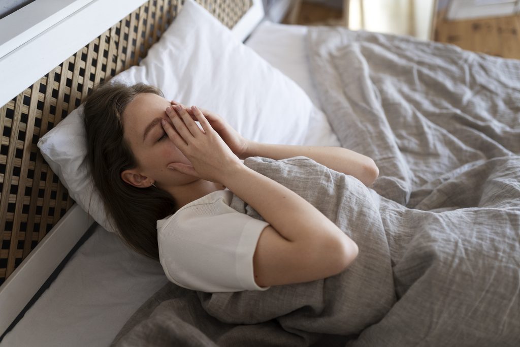 Femme allongée dans son lit la nuit, préoccupée par ses tâches et son organisation quotidienne.